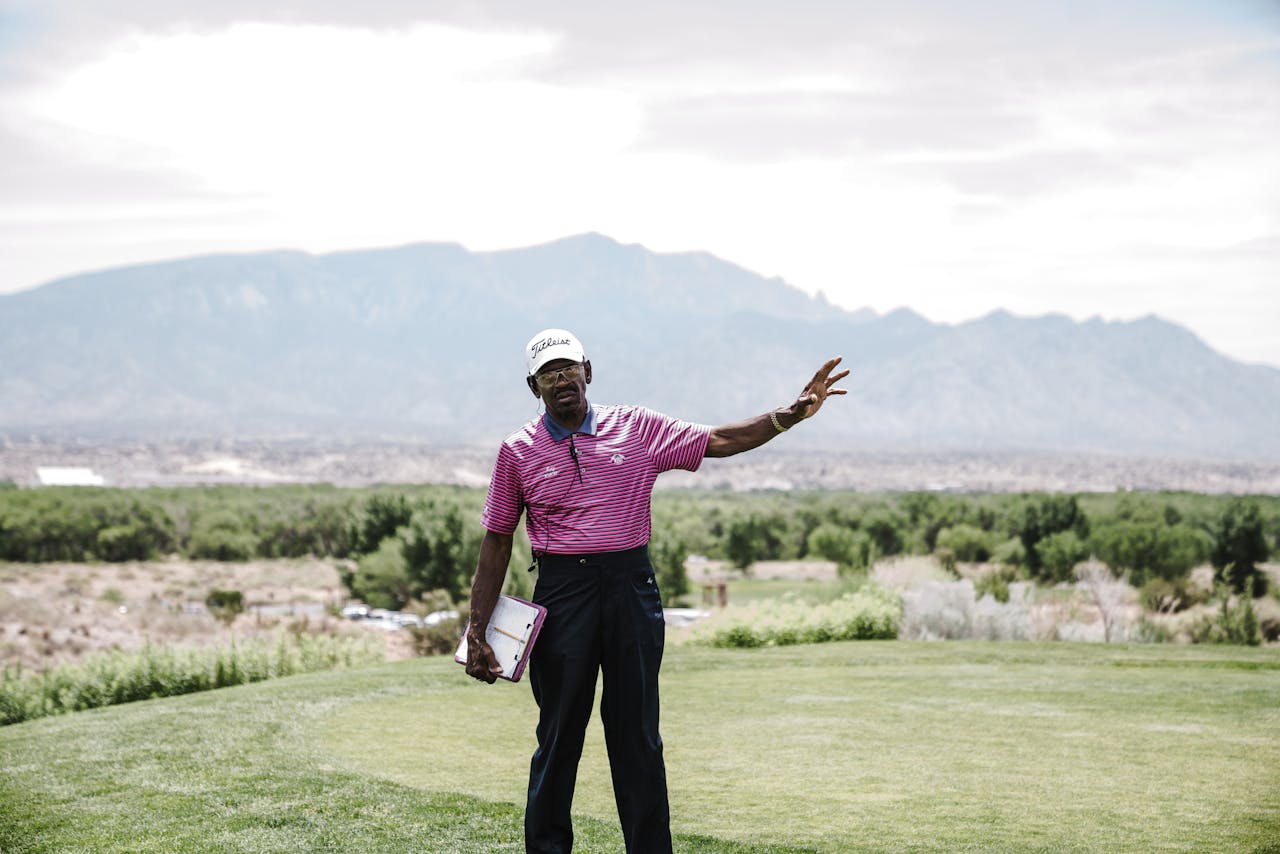 A golf caddie gestures on a scenic golf course with mountains in the background, exuding leisure and relaxation.