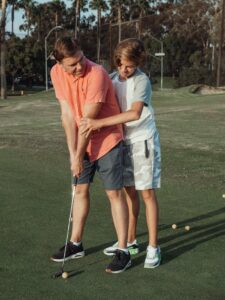 Father and son enjoy a bonding moment learning to play golf on a sunny day.